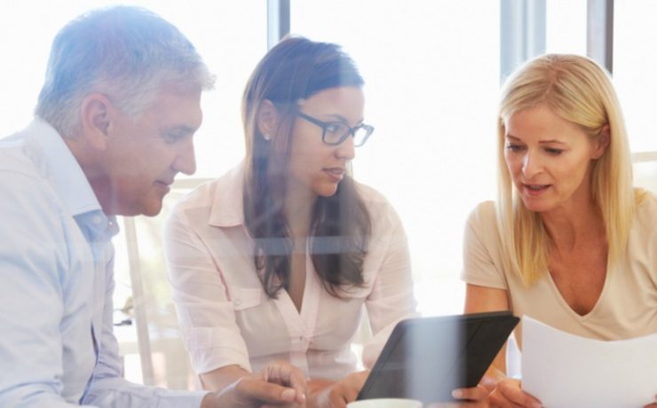 Three workers sitting around a desk looking at documents