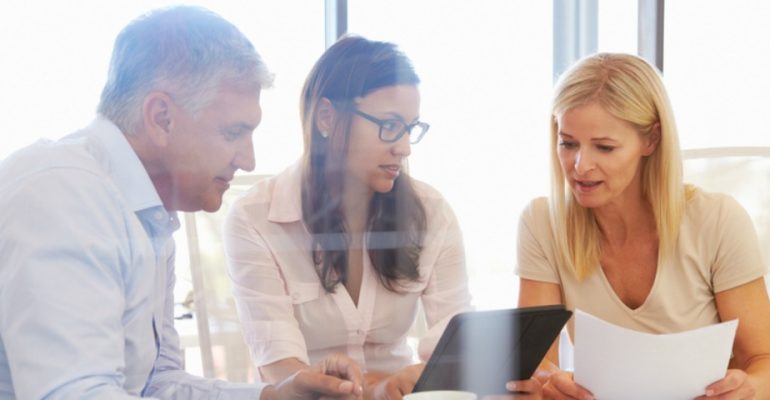 Three workers sitting around a desk looking at documents