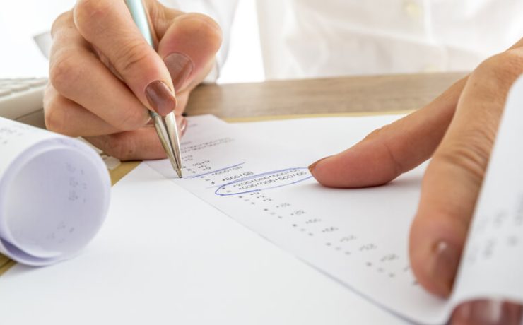 Close up Businesswoman Calculating Expenses on Printed Receipts at her Desk with Calculator on her Side.