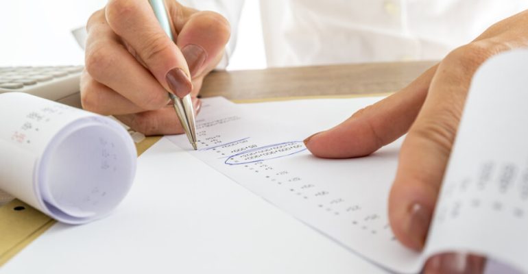 Close up Businesswoman Calculating Expenses on Printed Receipts at her Desk with Calculator on her Side.
