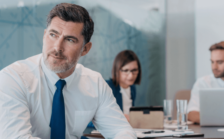 Business man sitting and thinking. Male and female coworker behind him.