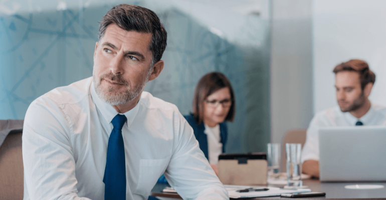 Business man sitting and thinking. Male and female coworker behind him.