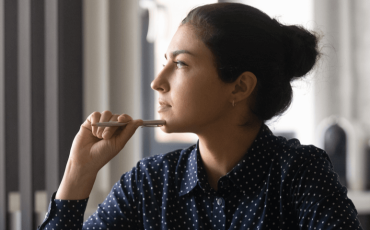 Young woman holding pen up to face, thinking about difficult decision