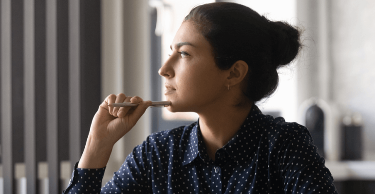 Young woman holding pen up to face, thinking about difficult decision