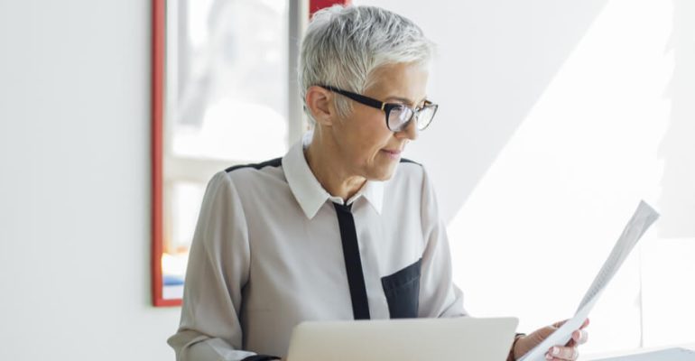 Female looking at paper while working on laptop