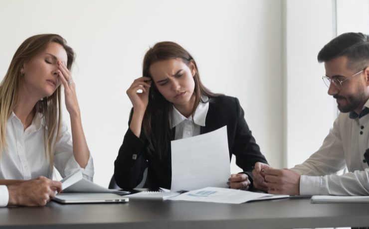 Group of business people sitting at conference table thinking with confused looks on face.