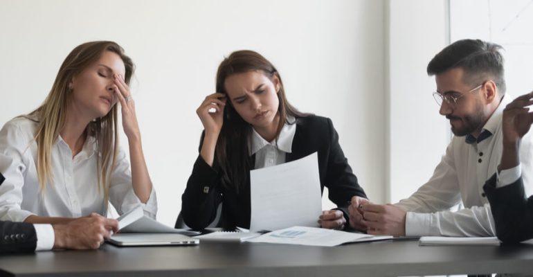 Group of business people sitting at conference table thinking with confused looks on face.