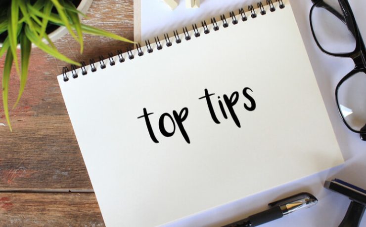 Notepad with the words 'top tips' written on it. Pair of reading glasses and plant next to notepad.