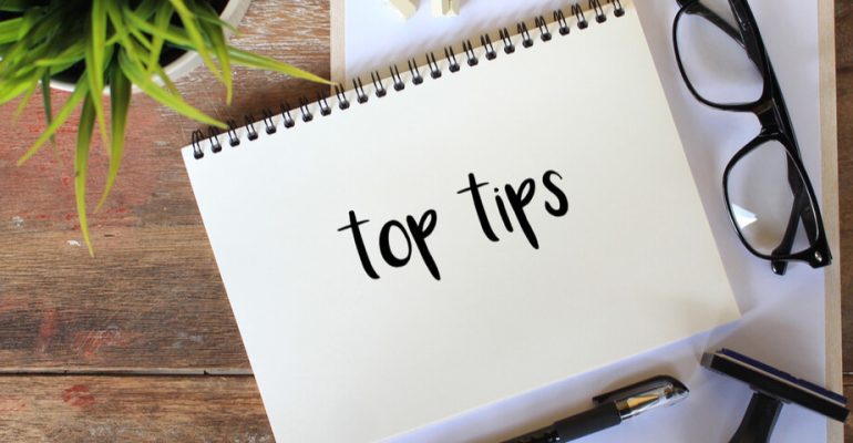 Notepad with the words 'top tips' written on it. Pair of reading glasses and plant next to notepad.