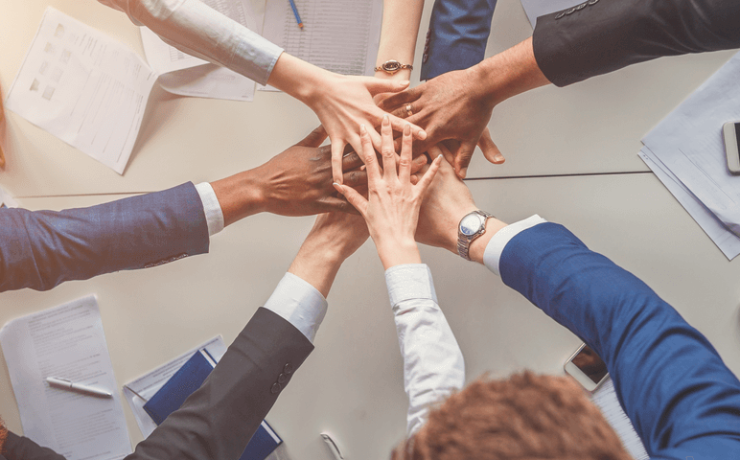 Group of business people in a circle extending their hands to have them all meet in the middle