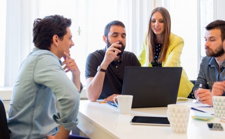 Four business people at a conference table looking at a laptop
