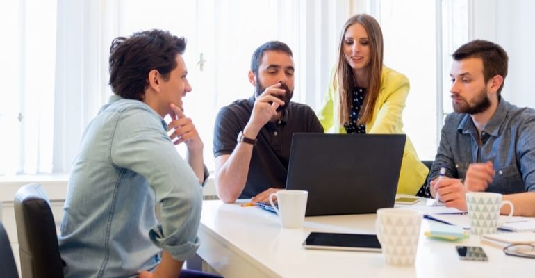 Four business people at a conference table looking at a laptop