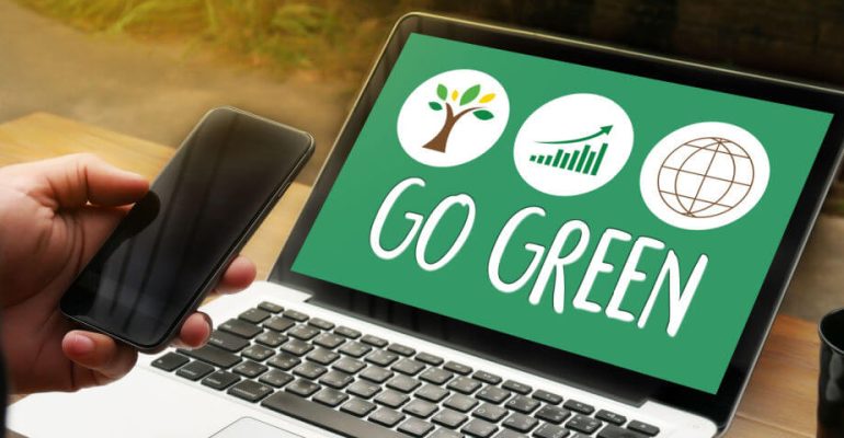 Open laptop with the words Go Green on the screen and a person's hand holding a smart phone