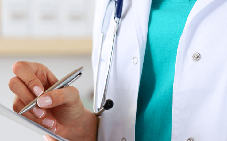 Doctor in a lab coat with a stethoscope around her neck filling out a chart