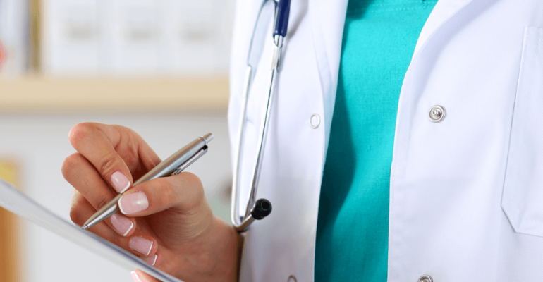 Doctor in a lab coat with a stethoscope around her neck filling out a chart