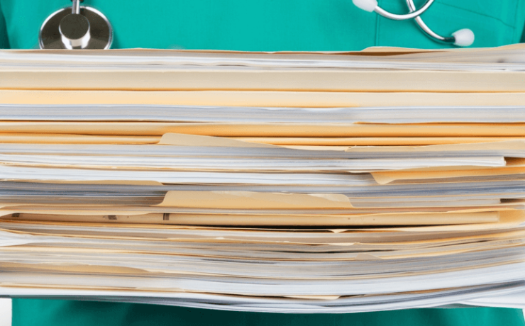 Medical professional with stethoscope around neck holding a large stack of documnets