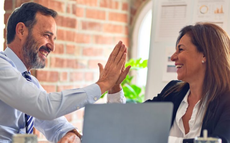 Two business people sitting at a desk in an office high-fiving each other
