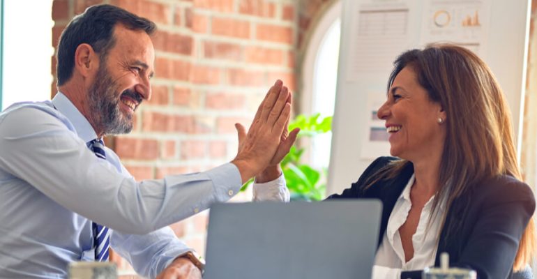 Two business people sitting at a desk in an office high-fiving each other