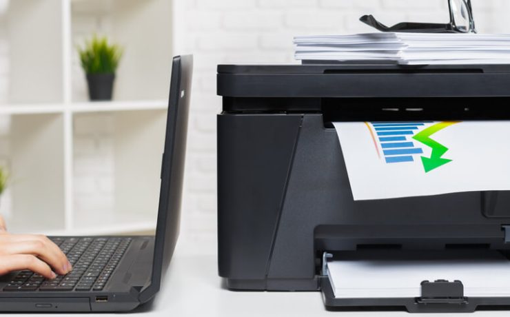 Hands working on a laptop with a a multifunction printer next to it