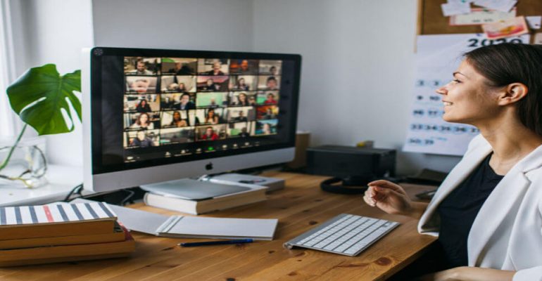 Woman at desk smiling having a video conference call with many people