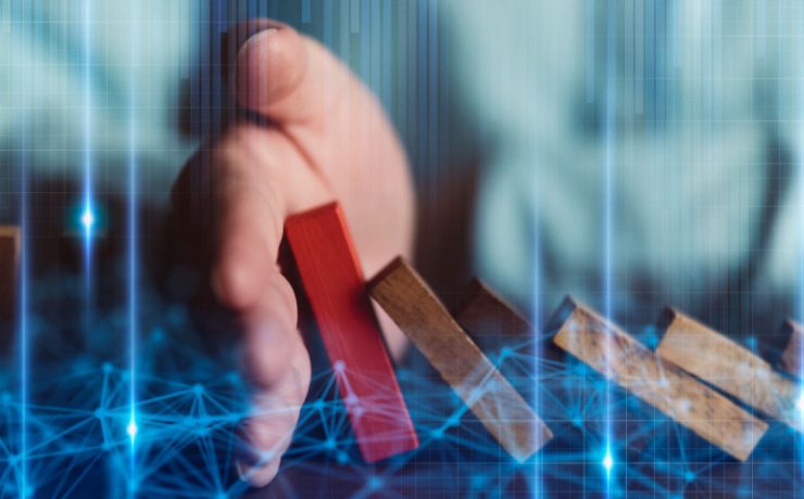 Hand stopping red wooden block being pushed over by brown wooden blocks
