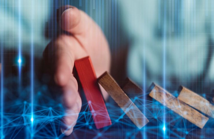 Hand stopping red wooden block being pushed over by brown wooden blocks