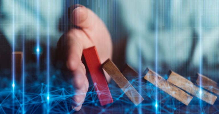 Hand stopping red wooden block being pushed over by brown wooden blocks