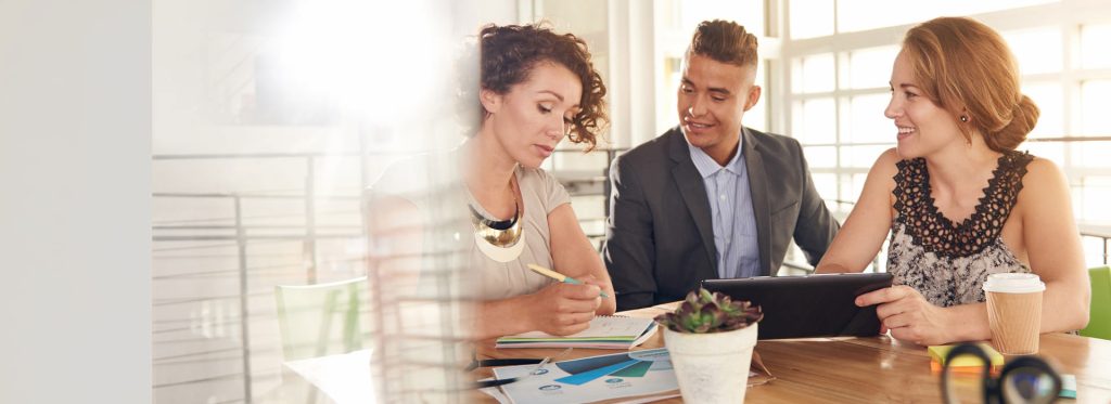 Three people sitting at a table working together and smiling