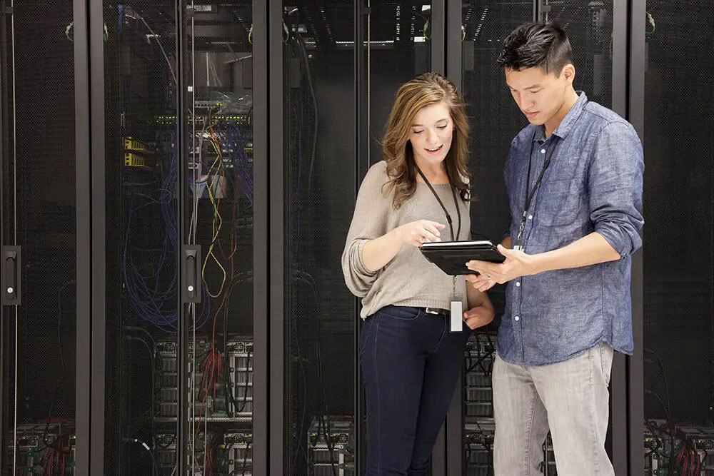 Two data center technicians standing in front of a server cabinet looking at a tablet