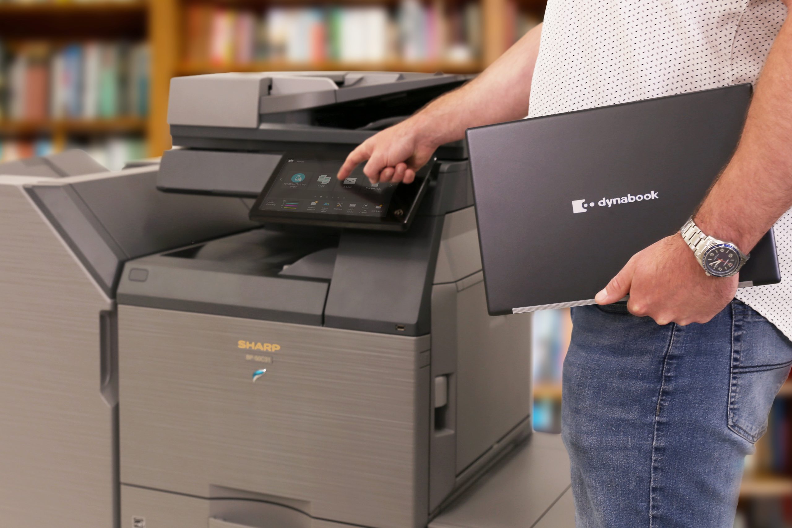 Man carrying laptop while printing at a multifunction printer. Image representing Business Equipment.