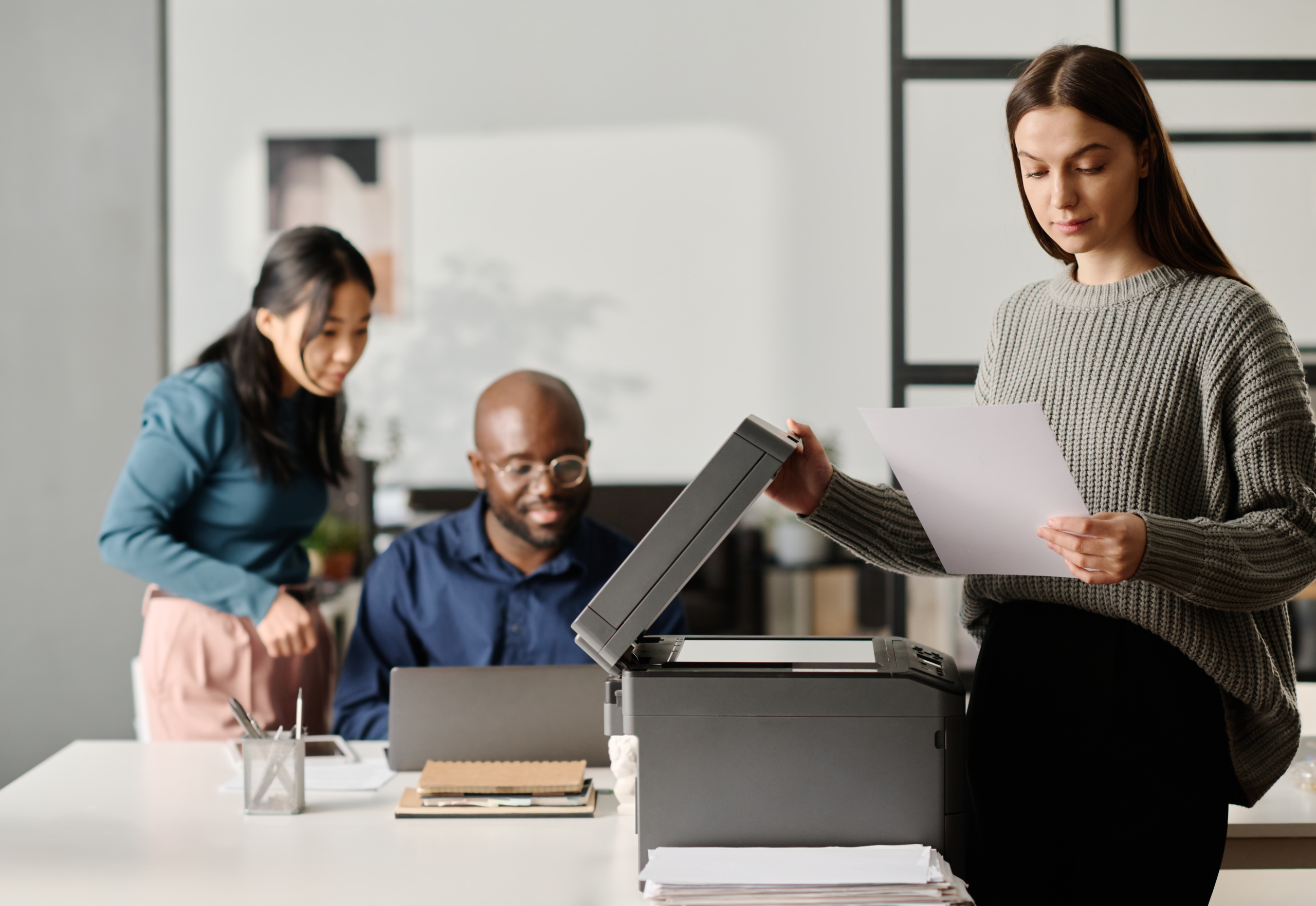 Three team members sitting around a desktop printer while one scans a document to cloud faxing.