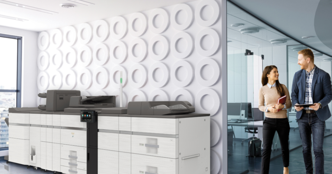 Sharp BP-80C80 production print device in a modern office with two employees talking nearby