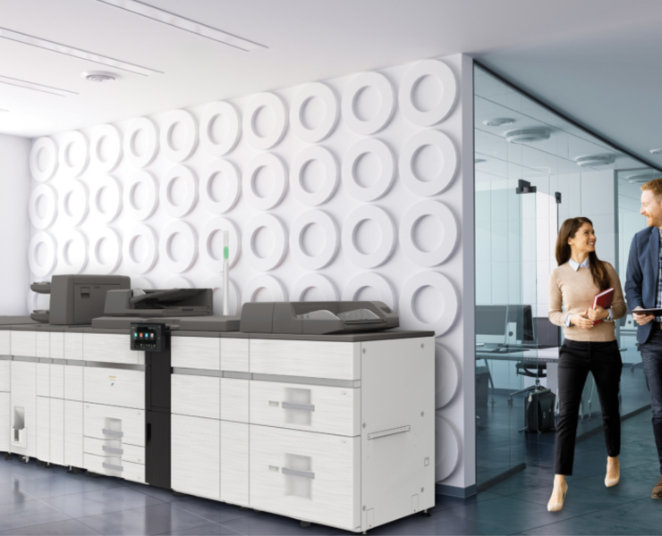 Sharp BP-80C80 production print device in a modern office with two employees talking nearby